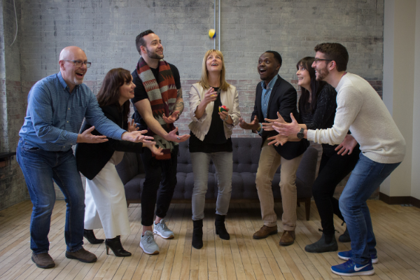 Michelle throwing a ball in the air with members of the Pillar team posing as if catching it